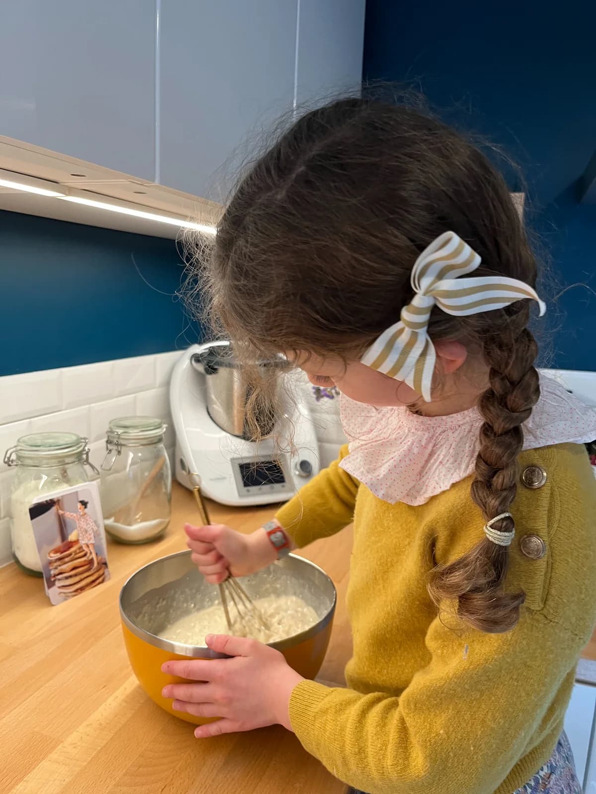 Crêpes, pull moutarde Petite fille préparant des crêpes, pull moutarde et nœud rayé doré — By Mésange