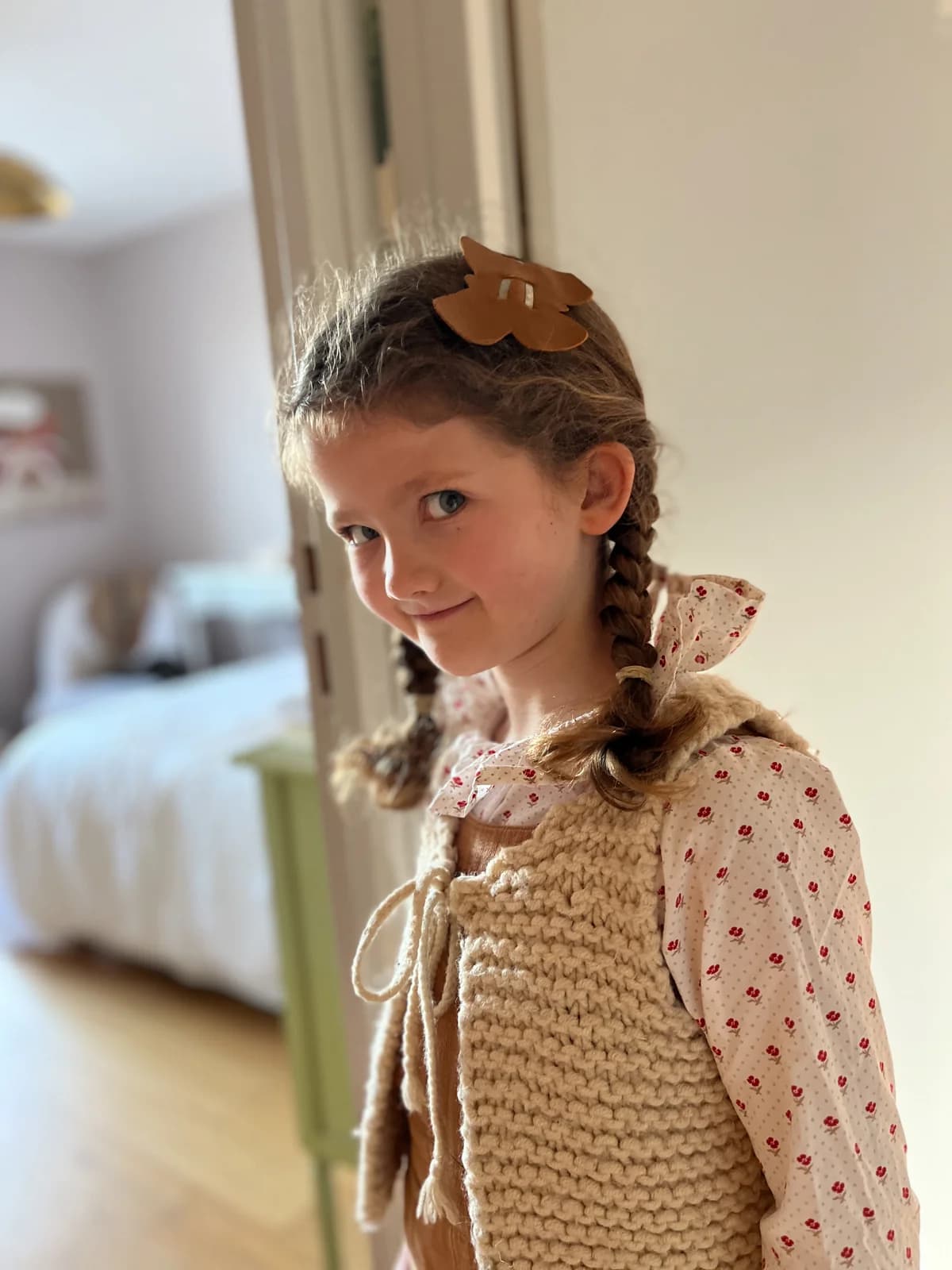 Gilet tricot, blouse smocks Fillette souriante en gilet tricot beige et blouse fleurie à smocks, barrette papillon — By Mésange